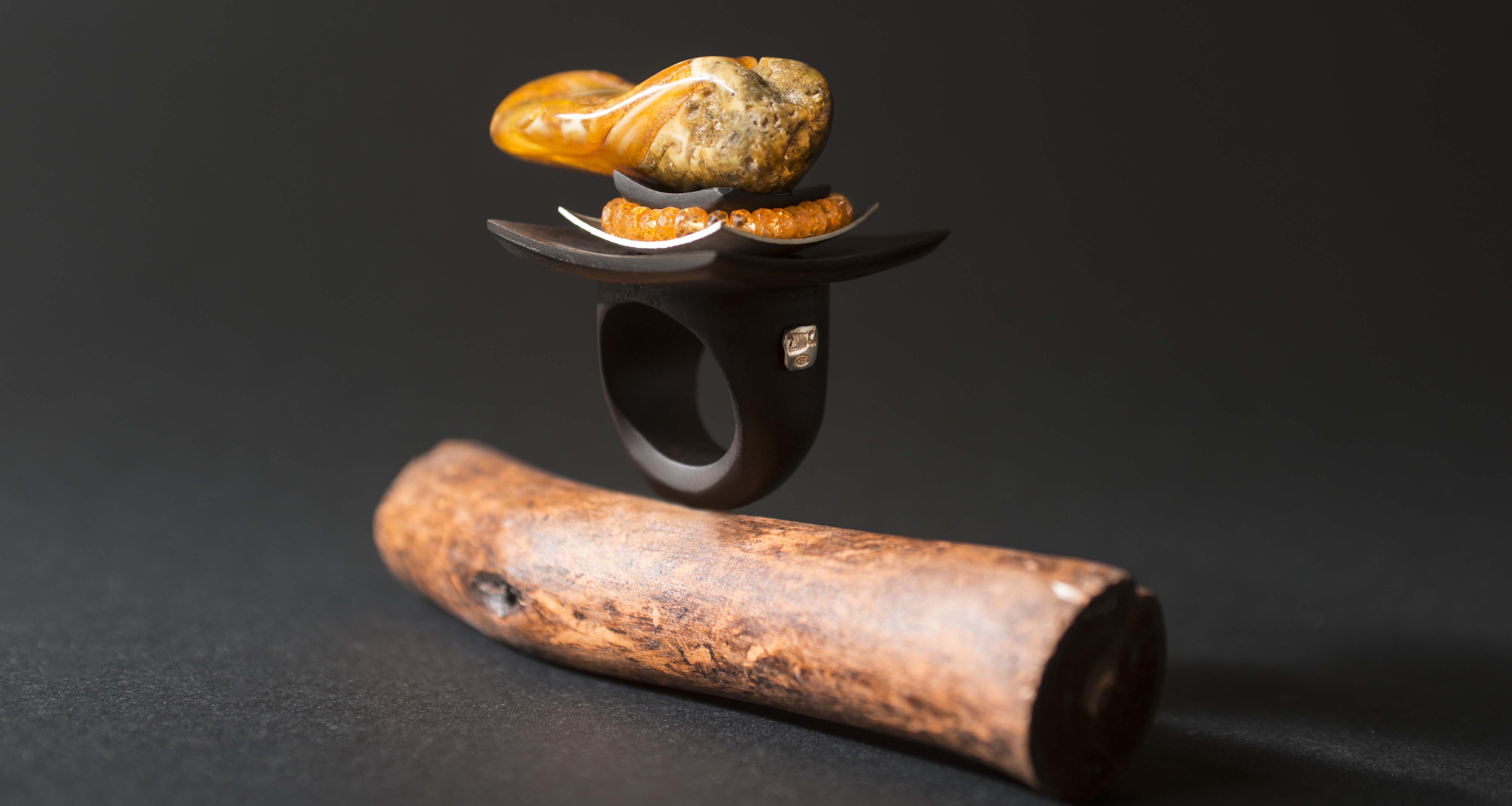 Anello in ebano con foglia d'argento contornata da granato spessartite con ambra baltica usata come punta della piramide.